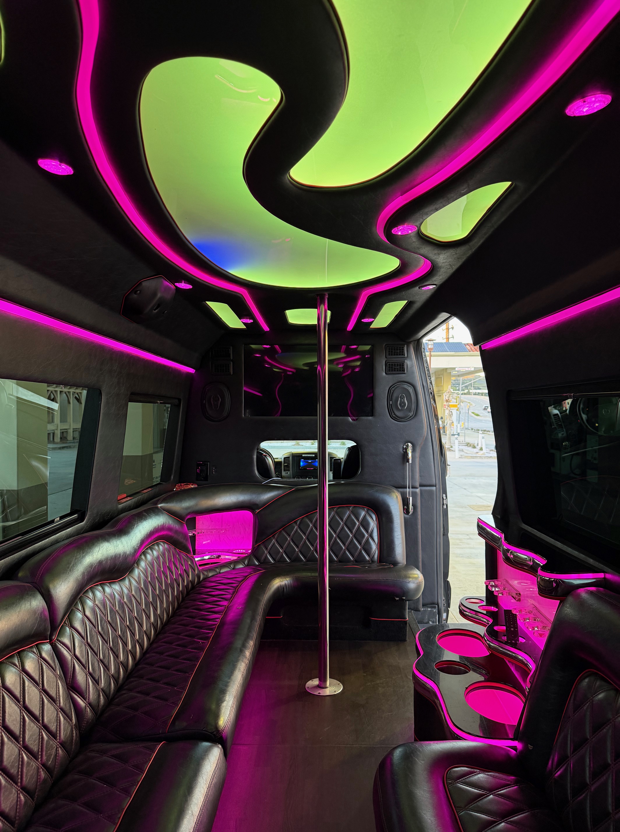 Interior of a stretch limousine featuring black leather seating, colorful lighting, and a center pole.